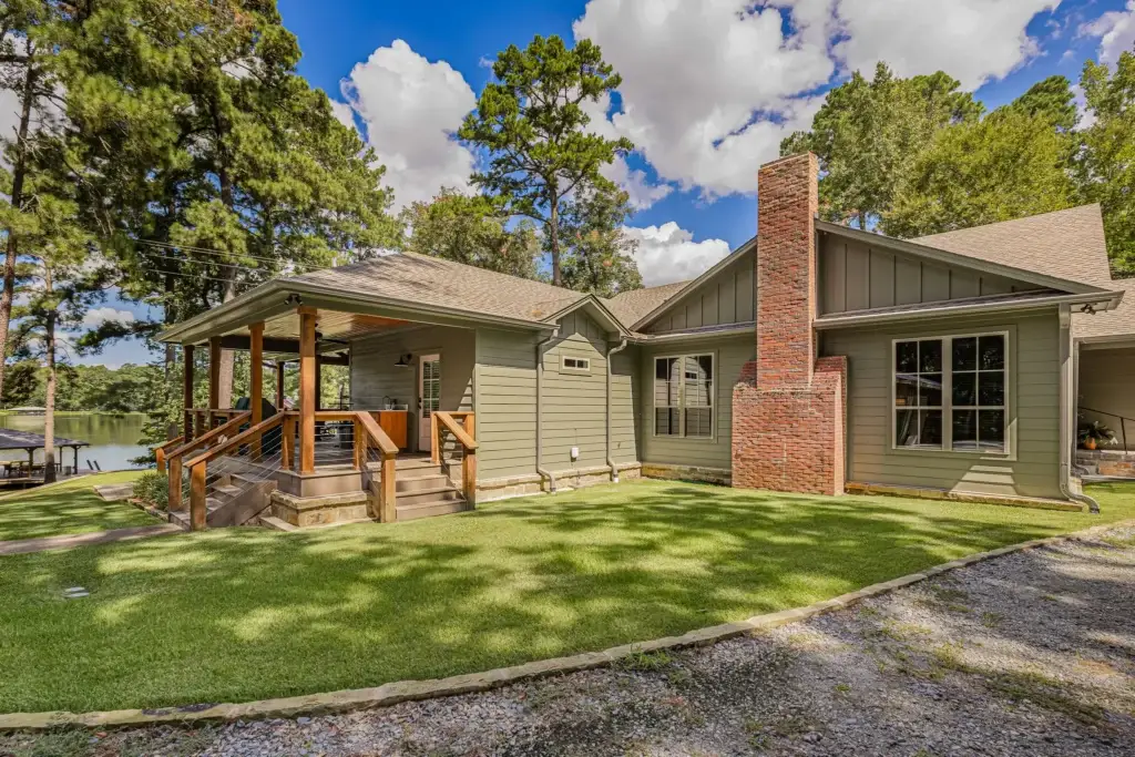 Side of the lake house with a brick chimney and the covered porch